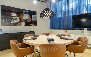 Modern conference room at Kennemerplein 6-14, Haarlem Centraal Station, featuring a round table with brown chairs, a flat-screen TV, and stylish lighting. Ideal for office space rental.