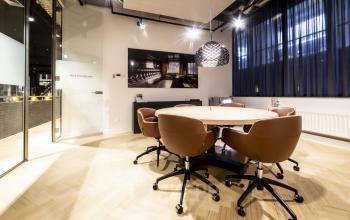 Modern conference room at Kennemerplein 6-14, Haarlem Centraal Station, with wooden flooring, round table, brown chairs, and stylish lighting. Office space rental available.