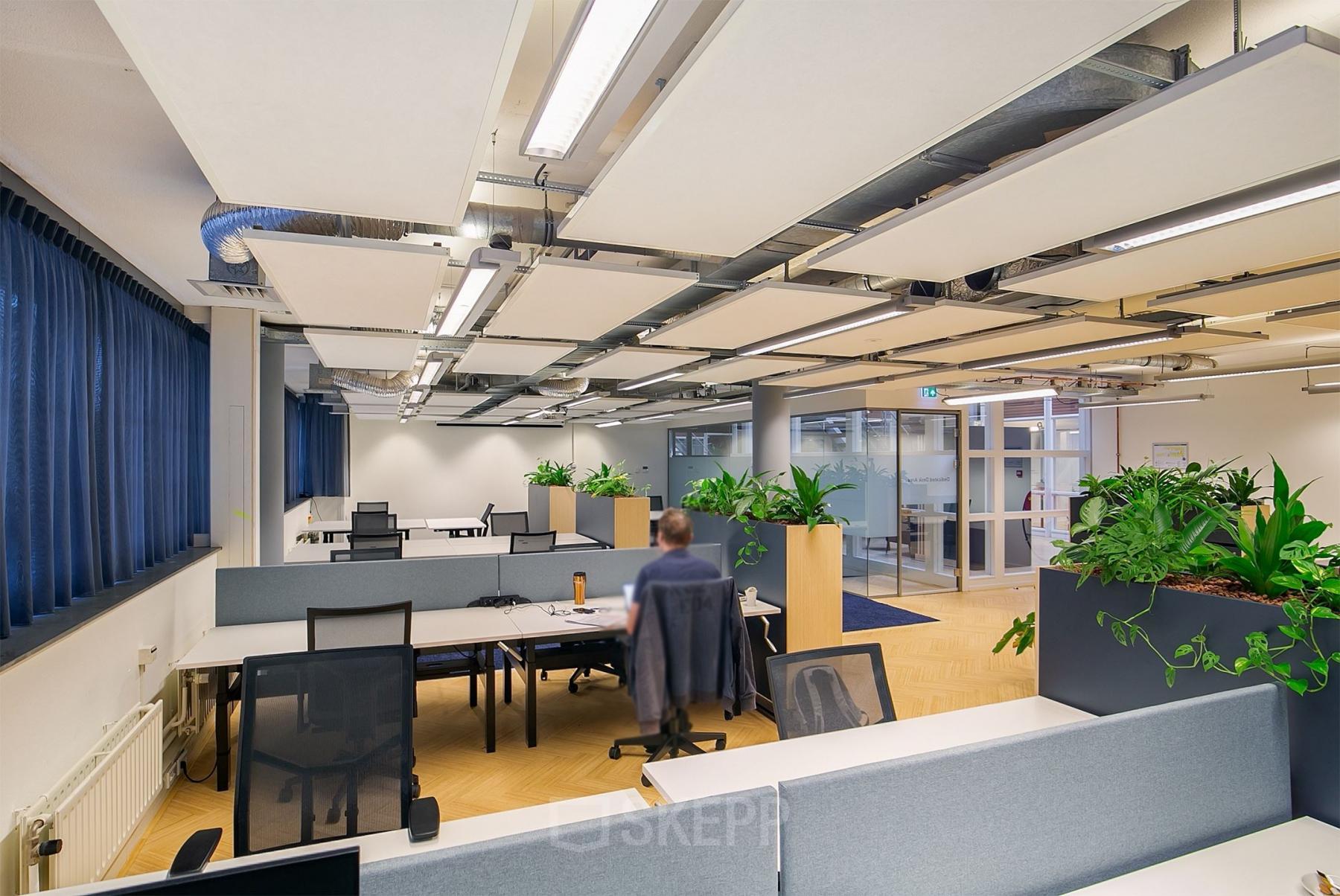 Modern office space at Kennemerplein 6-14, Haarlem Centraal Station, with desk partitions, chairs, and greenery, suitable for office space rental.