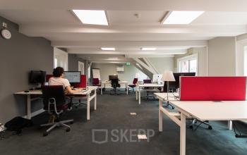 Modern office space rental at Nieuwe Gracht 3, Haarlem Centrum, with professionals working at organized workstations under bright lighting.