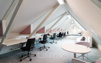 Open and well-lit office space rental at Nieuwe Gracht 3, Haarlem Centrum, featuring sleek desks and comfortable seating under angled ceilings with ample lighting.