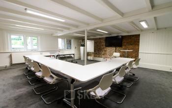 Modern office space rental at Nieuwe Gracht 3, Haarlem Centrum, featuring a large conference table, white chairs, and an exposed brick wall for a contemporary feel.