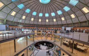 Spacious office to rent at Koepelplein 1E, Haarlem Centrum. Featuring a dome ceiling with abundant natural light, furnished workspaces and people engaged in discussions, ideal for office space rental.