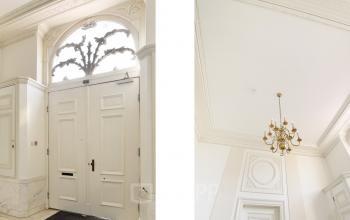 Entrance area of the office building at Nieuwe Gracht 74-76, Haarlem Centrum with a white door under an elaborative arch and a chandelier hanging from the ceiling.
