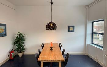 Bright, minimalist meeting room in Haarlem Oost with a long wooden table and eight chairs, suitable for office space rental.