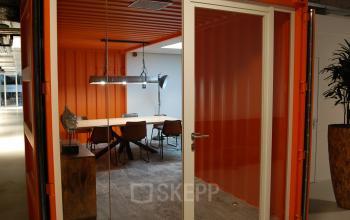 Office space rental with meeting room in vibrant orange container, featuring a wooden table, chairs, modern lighting, and decor, at A. Hofmanweg 5A, Haarlem Waarderpolder, Haarlem.