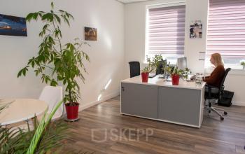 A bright office to rent with a person working at a desk surrounded by plants, featuring modern furnishings at Waarderweg 19, Haarlem Waarderpolder.