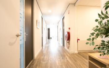 View of a well-lit hallway in an office space available for rent at Waarderweg 19, Haarlem Waarderpolder, featuring wooden flooring and framed prints on the walls.