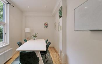 Interior of an office space at Florapark 7, Haarlem Zuid, Haarlem, featuring a meeting table with green chairs, a whiteboard, and modern decor pieces.