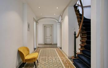 Entrance hall of the office building at Florapark 7, Haarlem Zuid, Haarlem with elegant tiled flooring, a yellow chair, and a winding staircase.