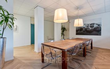 Spacious office area for rent at Fonteinlaan 5, Haarlem Zuid, with modern wooden table, clear chairs, contemporary artwork, and hanging lights.