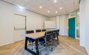 Conference room at Fonteinlaan 5 in Haarlem Zuid with a large wooden table, black chairs, modern lighting, and a whiteboard.
