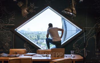 A professional in a stylishly designed office space for rent at Suikersilo Oost-West 1-41, Halfweg, gazes out a large window, reflecting creative thinking.