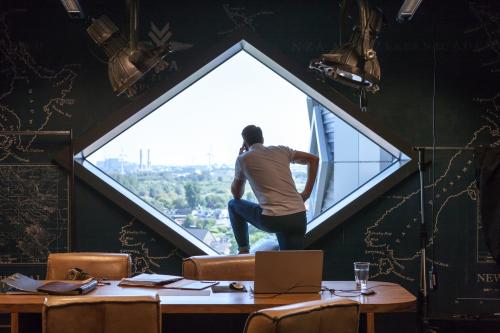 A professional in a stylishly designed office space for rent at Suikersilo Oost-West 1-41, Halfweg, gazes out a large window, reflecting creative thinking.
