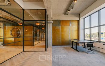 Modern office interior located at Haarlemmerstraatweg 13, Halfweg, featuring stylish glass walls and spacious windows. Ideal for office space rental with a blend of carpeted and wood flooring for a versatile workspace.