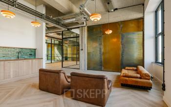 Modern office space with brown leather seating and a unique wall design, featuring a kitchenette area and stylish lighting. Ideal for rent office space enthusiasts seeking a contemporary environment.