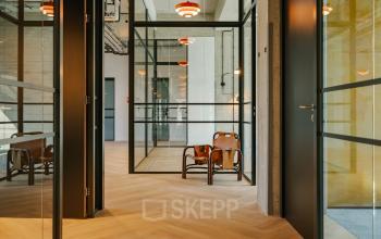 Office space rental at Haarlemmerstraatweg 13, Halfweg featuring a modern, glass-enclosed workspace with sleek wooden flooring and stylish seating area.