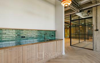 Modern interior of office space at Haarlemmerstraatweg 13, Halfweg, featuring a sleek kitchenette with wooden cabinets and a green tiled backsplash, perfect for office space rental.