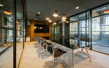 Modern office space for rent at Haarlemmerstraatweg 13 featuring a sleek conference room with a long glass table and stylish chairs, set against glass walls and warm lighting.