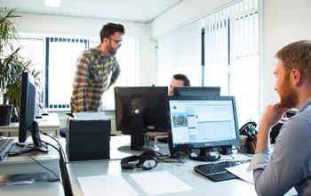 Modern office space rental at Haarlemmerstraatweg 7, Halfweg with three people working at desks and computers, plants, and large windows providing natural light.