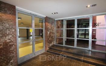 Interior view of office space at Haarlemmerstraatweg 11, Halfweg, featuring modern glass doors, brick walls, and tiled flooring.