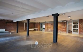 Spacious interior of an office to rent at Haarlemmerstraatweg 11 in Halfweg, featuring exposed brick walls and large open floor space.