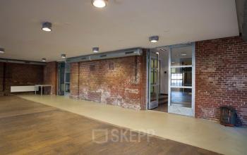 Office space rental at Haarlemmerstraatweg 11 in Halfweg, featuring exposed brick walls, wooden flooring, and modern ceiling lights.