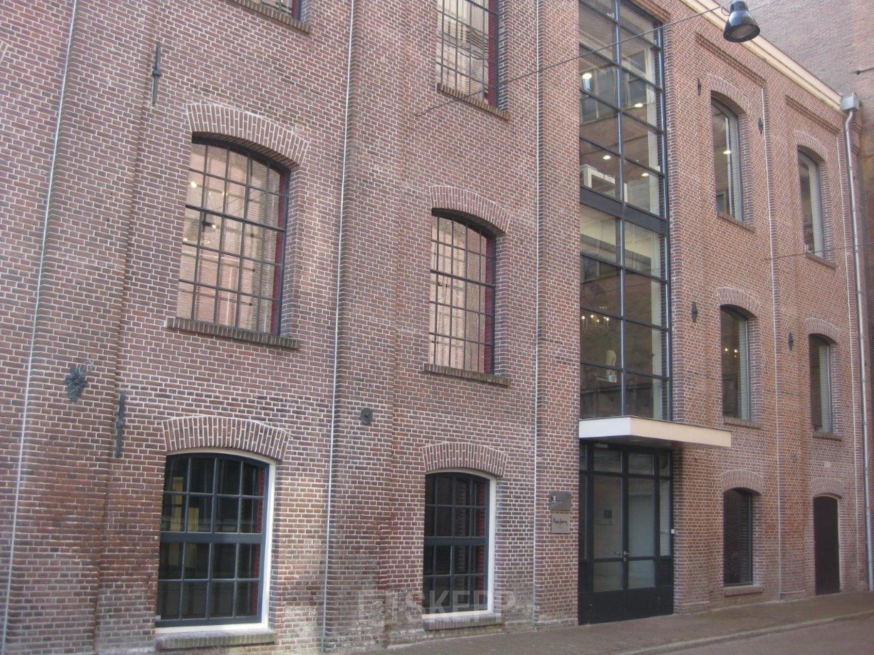 Exterior view of the brick office building located at Haarlemmerstraatweg 11, Halfweg. Large windows and a glass entrance highlight the facade, an attractive setting for office space rental.