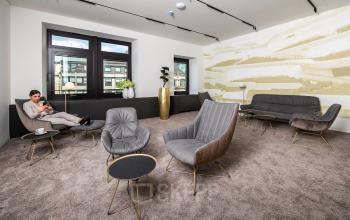 Gemütlicher Besprechungsraum im Bürogebäude Ballindamm 27, Hamburg Altstadt, mit modernen Sitzgelegenheiten und großer Fensterfront. Eine Frau arbeitet konzentriert an einem Laptop, ein ansprechender Ort zum Bürofläche mieten.