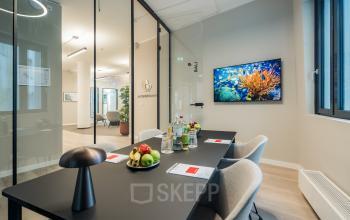Modern conference room with a sleek black table, beige chairs, and a wall-mounted screen at Überseeallee 1, Hamburg Hafencity, suitable for office space rental.