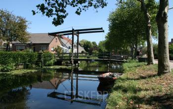 Reflective view of a serene canal near the office space rental at Techniekweg 2, Harmelen, with green surroundings and a quaint bridge.