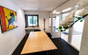 Furnished office space for rent at Herenweg 115 in Heemstede, featuring a long table, chairs, and a vibrant wall painting.
