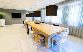 Spacious office with a long wooden table and chairs at Herenweg 115, ideal for office space rental. Bright lighting and minimalist decor highlight this attractive workspace.