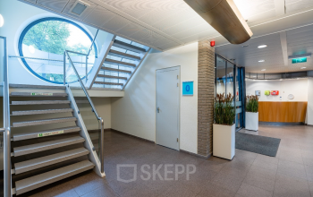 Modern office entrance at Geerstraat 115, Heerlen, featuring sleek stairs, circular window, and inviting welcome area. Ideal for office space rental.