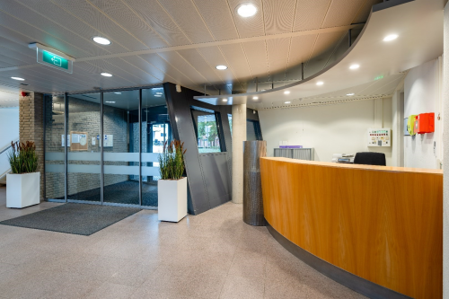 Modern office reception area at Geerstraat 115, Heerlen, featuring a sleek wooden desk and glass entrance doors, perfect for welcoming visitors. Ideal office space rental opportunity.