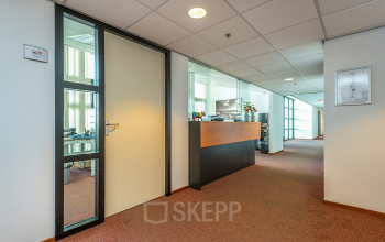 Interior view of an office space rental at Milaanstraat 70-110, Heerlen, featuring a carpeted hallway with doors leading to private offices. The area is well-lit with modern finishes and decor.