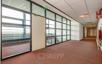 Spacious office hallway at Milaanstraat 70-110 in Heerlen, featuring large glass windows overlooking a staircase. Ideal for office space rental with a professional yet inviting atmosphere.