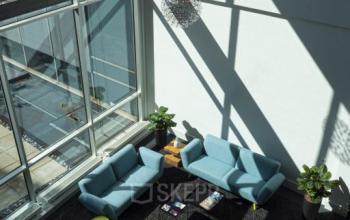 Bright office lounge area with modern furniture, featuring blue sofas and yellow chairs at Snellius 1, Heerlen. Ideal for office space rental.