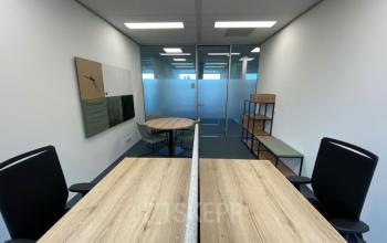 Modern office space rental at Snellius 1, Heerlen, featuring work desks, chairs, shelving units, and a small meeting table within a well-lit interior.