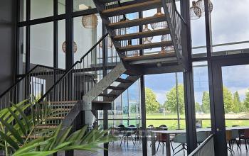 Modern office interior at Snellius 1 in Heerlen with a stylish staircase, large windows, and natural lighting. The space features a view of greenery outside, ideal for an inviting office space rental.