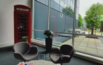 Bright office interior with modern furniture at Snellius 1 in Heerlen, large windows, and a red British phone booth. Ideal for office space rental.