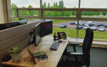 Modern office to rent at Snellius 1 in Heerlen, featuring a desk with a computer, chair, and a view of the parking area through large windows.