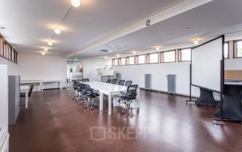 Spacious office space rental at Oliemolenstraat 60, Heerlen, featuring multiple desks, chairs, and a projector screen for presentations.