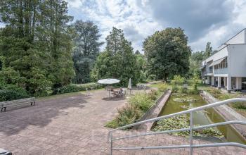Exterior of the office building at Oliemolenstraat 60, Heerlen, featuring a large patio area with outdoor seating and a pond.