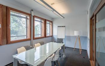 Bright office space to rent in Heerlen at Oliemolenstraat 60, featuring large windows, a glass table with white chairs, and a flip chart.