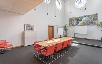 Spacious conference room at Oliemolenstraat 60 in Heerlen, featuring a large wooden table, red chairs, a whiteboard, and modern lighting.