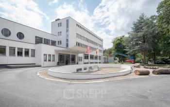 Exterior view of office building at Oliemolenstraat 60 in Heerlen, featuring multiple flags and a circular driveway.