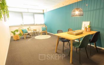 Bright office space at Steenovenweg 5, Helmond featuring a large window, stylish chairs, a wooden table, and decorative plants.