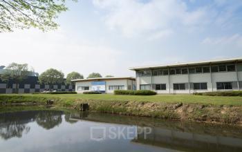Exterior view of an office building at Steenovenweg 5, Helmond, with green lawns and a pond in the foreground.