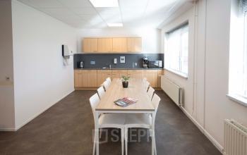 Bright office kitchen with a long table and eight chairs, located at Steenovenweg 5, Helmond, ideal for office space rental.